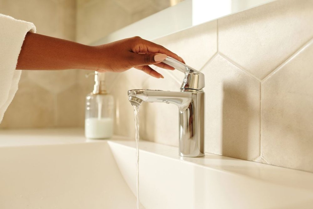 Hand turning off a running mixer tap above a bathroom basin Hand turning off a running chrome mixer tap above a bathroom basin